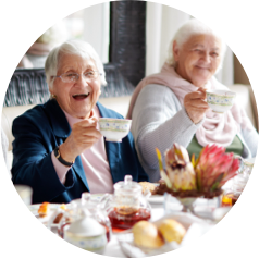 Elderly women enjoying tea together at a beautifully set table with pastries and flowers.