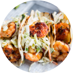 Grilled shrimp tacos topped with shredded cabbage and cilantro in soft tortilla shells.