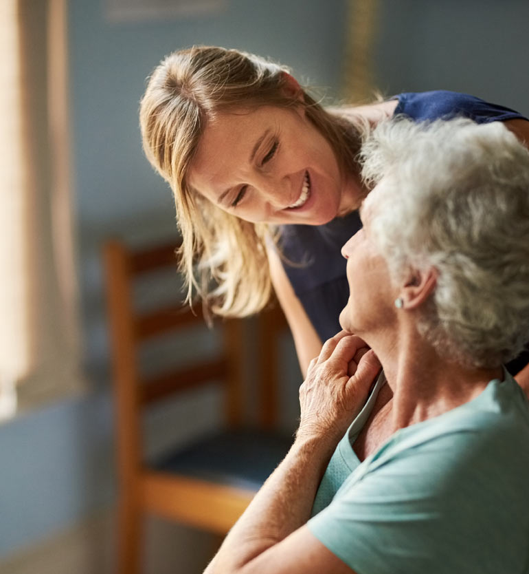 Caregiver smiling warmly over the shoulder of senior woman.