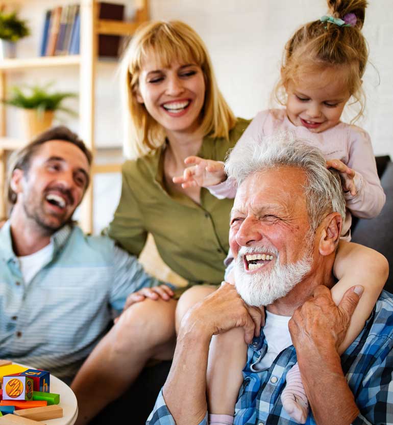 Senior man joyfully playing with family, including young child on his shoulders, laughing together.