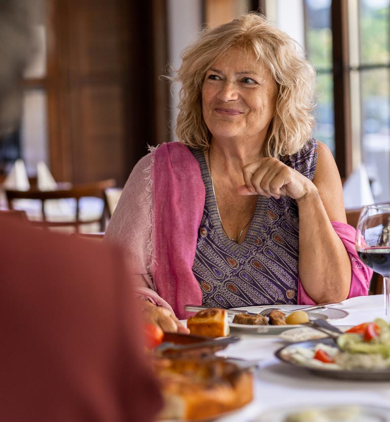 Senior woman smiling and dining with friends in a restaurant, enjoying a meal and conversation.