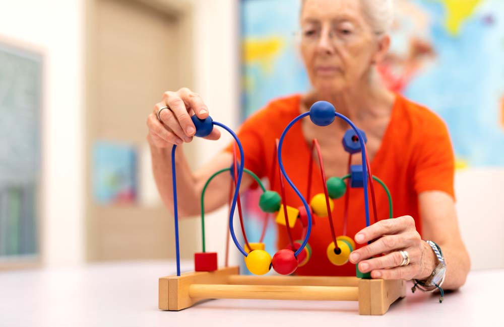Senior woman engaging in a cognitive activity with a bead maze toy during a memory care session.
